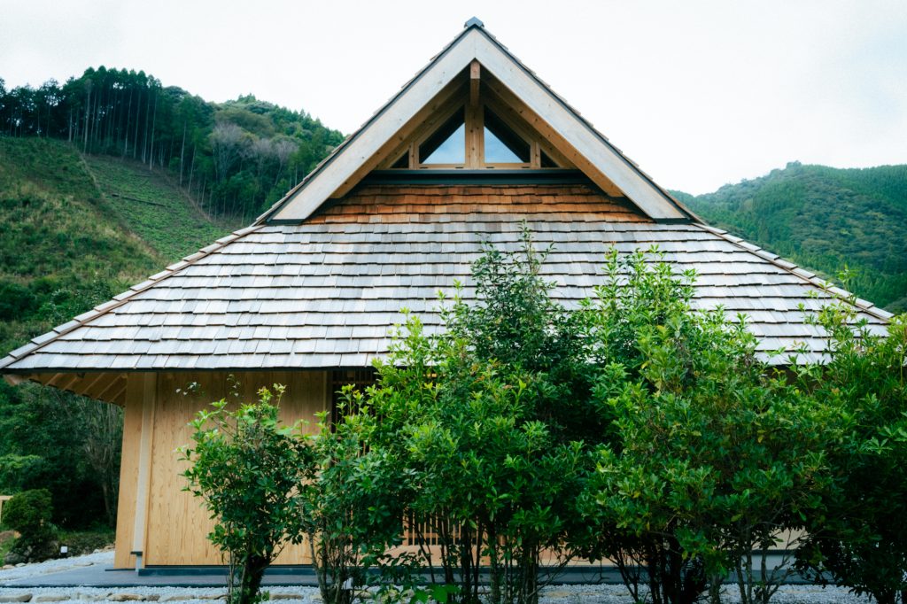 ザイツ建築の手がけた佐伯市にある住宅の外観、家の手前には植栽成人男性ほどの高さ、屋根はとても大きくレッドシダー材のハンドスプリントの屋根材を使用した入り母屋屋根