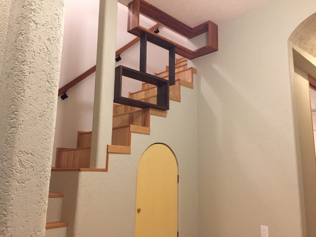 ザイツ建築の手がけた大分県日田市にある住宅の玄関から２階への階段、階段は４段目からストリップで落下防止に、異なるサイズの木箱を三つ組み合わせ天井まで設置、階段側からも玄関側からでもディスプレイ用の棚にも使用できる、階段下には収納がありクリーム色のドア付き、壁は左官仕上げ