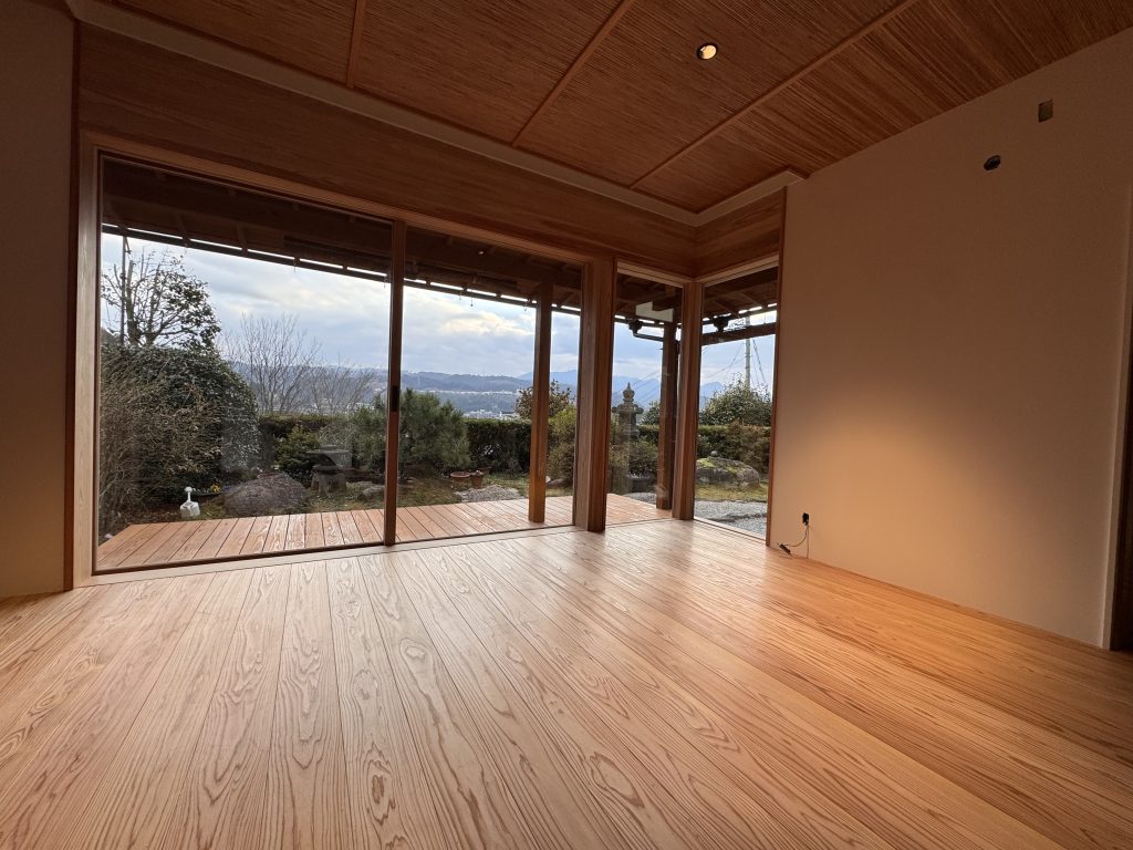 ザイツ建築株式会社が手がけたリフォーム工事の完成写真、床は大分県日田市産の無節赤身のみの杉のフローリング、天井は葦簀を敷き詰め等間隔で竿ぶちが窓に向かって配置、窓は木製で２枚引き違い窓高さは大きく成人男性の身長を超えるその横にL型でフィックス窓が並ぶ写真