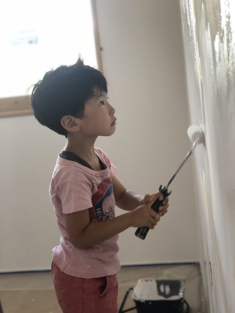 ザイツ建築株式会社のモデルハウス「てるおかの家」の壁に天然素材の塗料をローラーで塗装に挑戦する5歳の男の子の写真